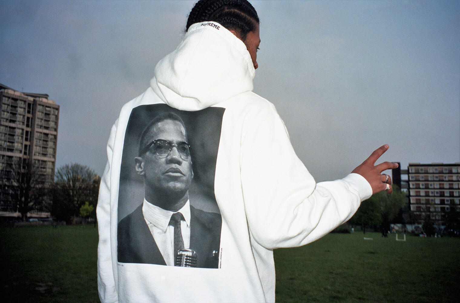 A photograph of a hoodie by Supreme being worn by a model, featuring a photograph of Malcolm X by Roy DeCarava.