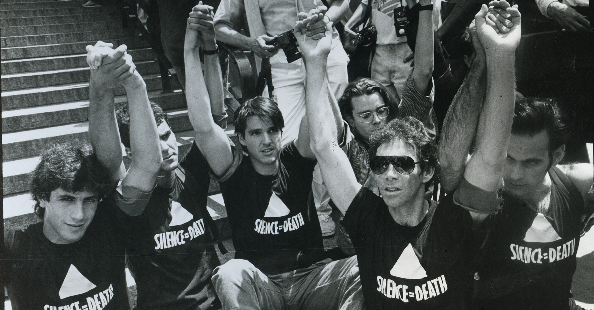 A detail from a photo by Donna Binder of the ACT UP Demo Federal Plaza NYC June 30, 1987 From left: Steve Gendon, Mark Aurigemma, Douglas Montgomery, Charles Stinson, Frank O’Dowd, Avram Finkelstein.
