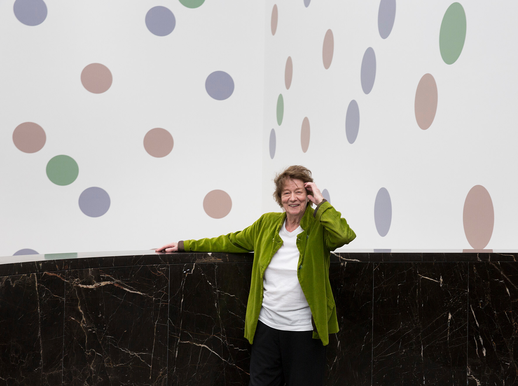 A photograph of Bridget Riley in front of her mural titled Messengers at The National Gallery in London, dated 2018.